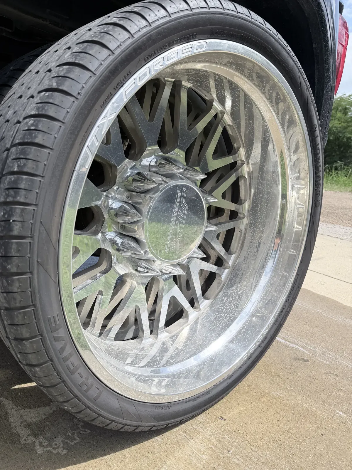 Polished forged aluminum wheel on a black pickup speckled with water spots and road film before wheel detailing