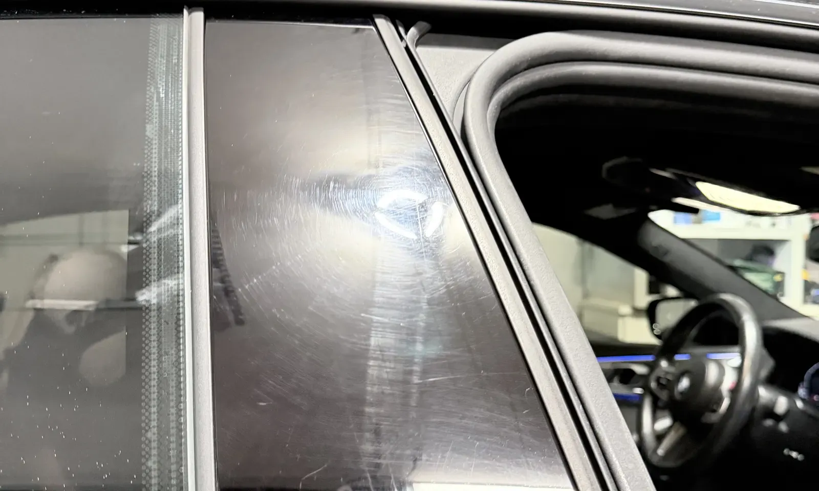 Swirl marks and fine scratches visible across gloss black BMW pillar trim before paint correction