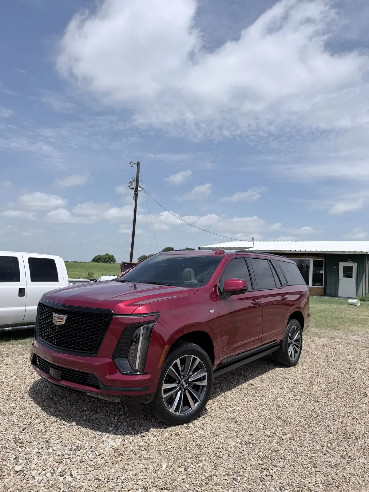 Deep red current-generation Cadillac Escalade with glossy detailed paint parked on a gravel drive under a blue Texas sky