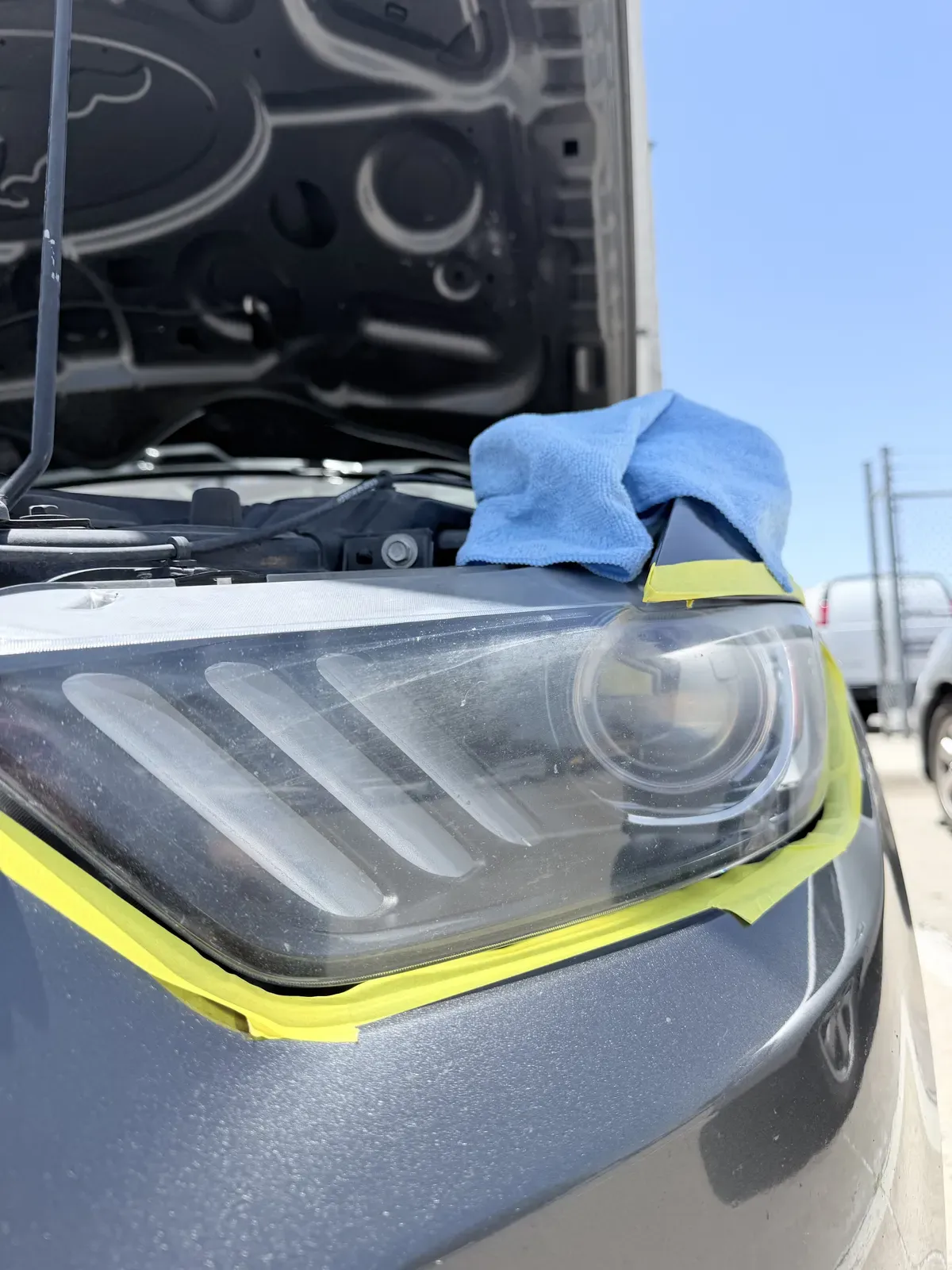 Ford Mustang headlight with surrounding paint masked off before wet sanding during mobile headlight restoration