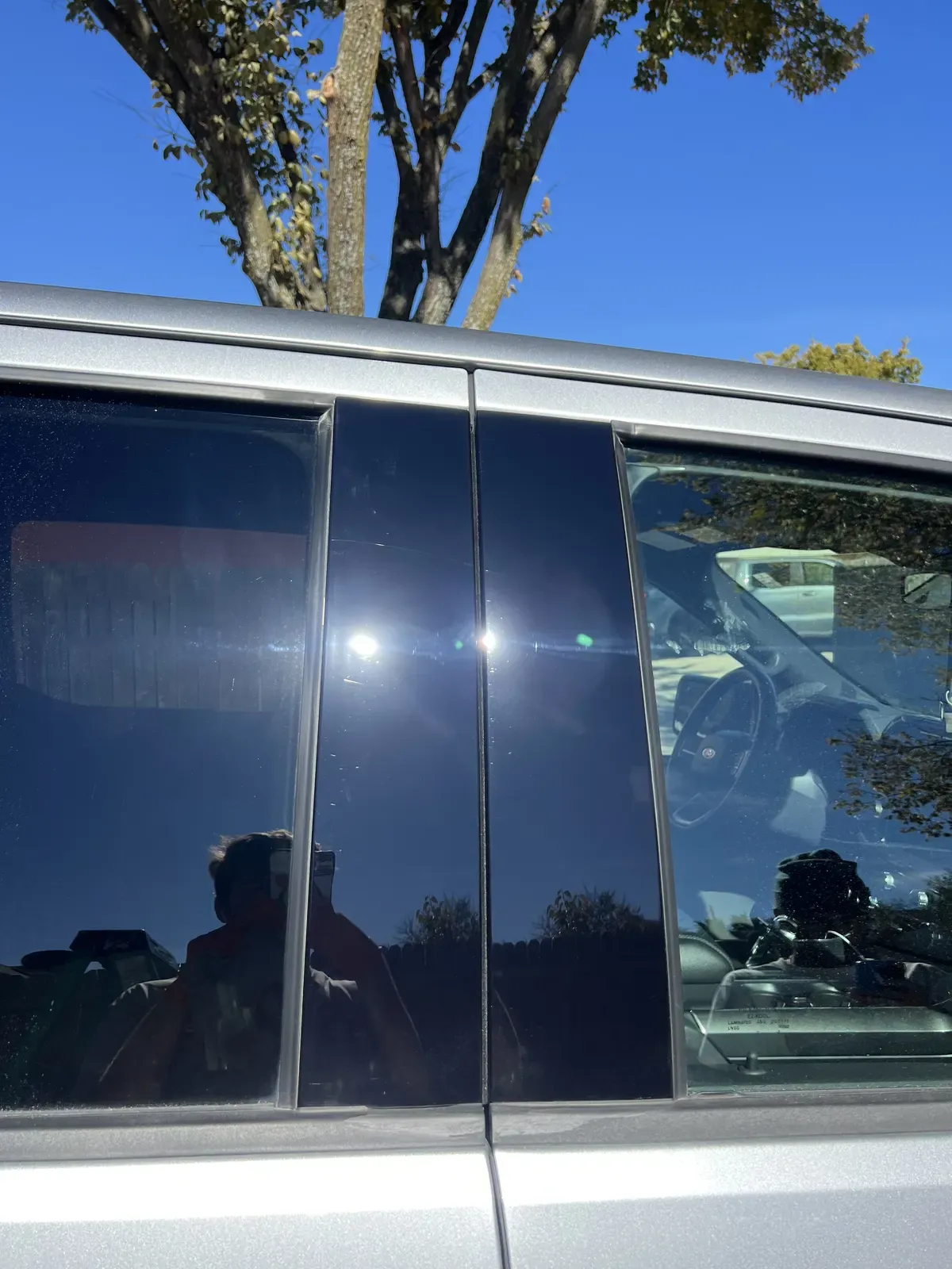 Corrected gloss black pillar trim throwing a single clean sun flare after paint correction